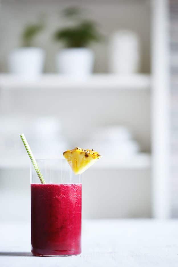 Beet and pineapple juice in a short glass, bright magenta, with a pineapple wedge and a striped paper straw