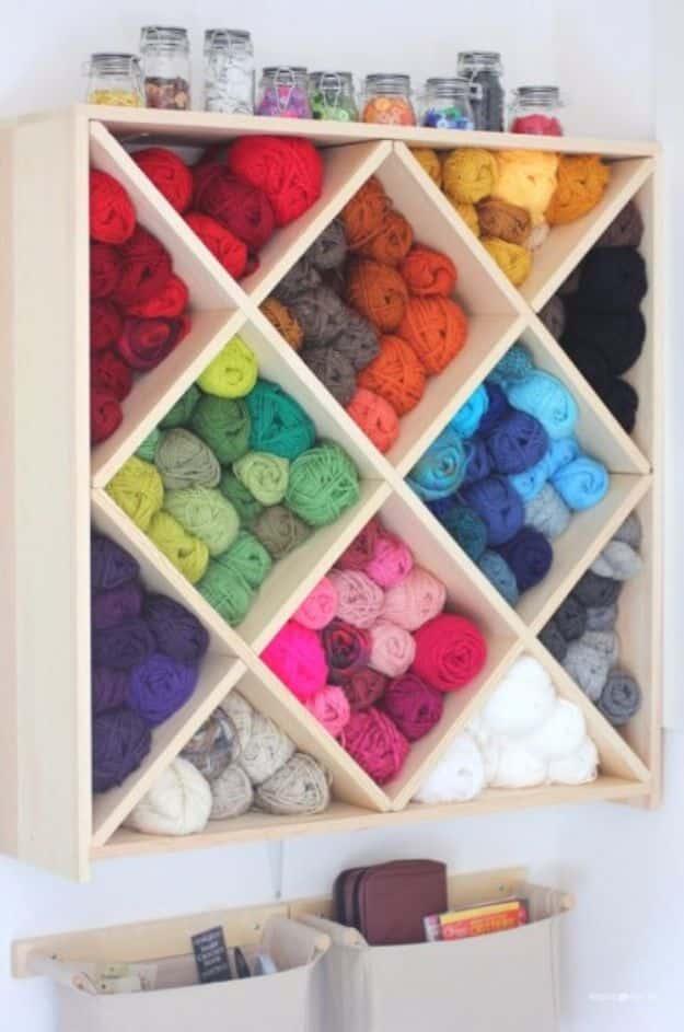 Wall mounted wooden wine rack with twelve diamond cubbies packed with yarn skeins sorted into rainbow order
