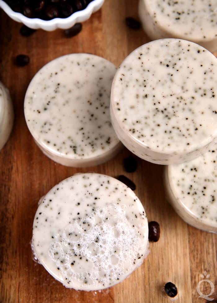 Round cream colored soap bars speckled with coffee grounds on a wood board with a small bowl of coffee beans