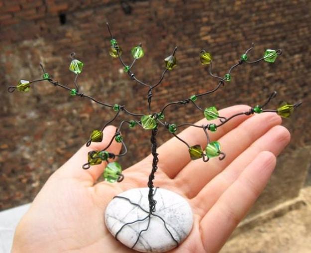 Wire gem tree with green faceted glass beads, its black wire roots wrapped around a white pebble, held in a palm