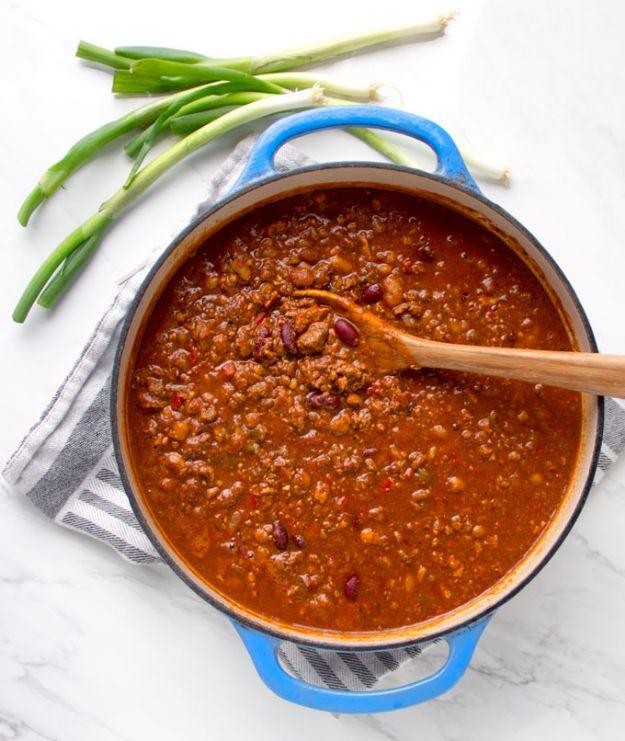 Award winning beef chili in a blue enamel pot with a wooden spoon and green onions on a marble counter