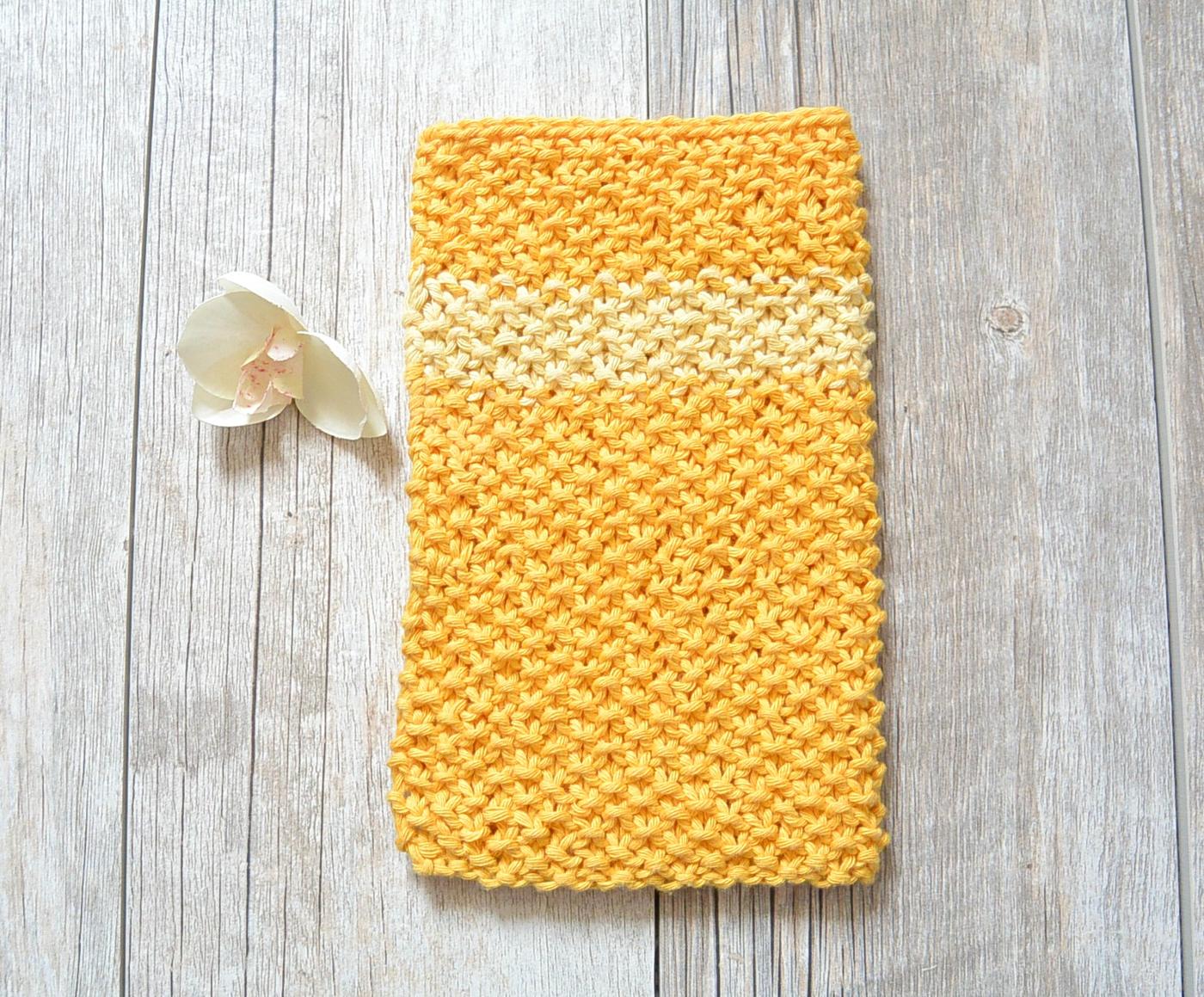 Yellow knit washcloth with a pale yellow stripe and a nubby seed stitch texture lying flat on weathered gray wood