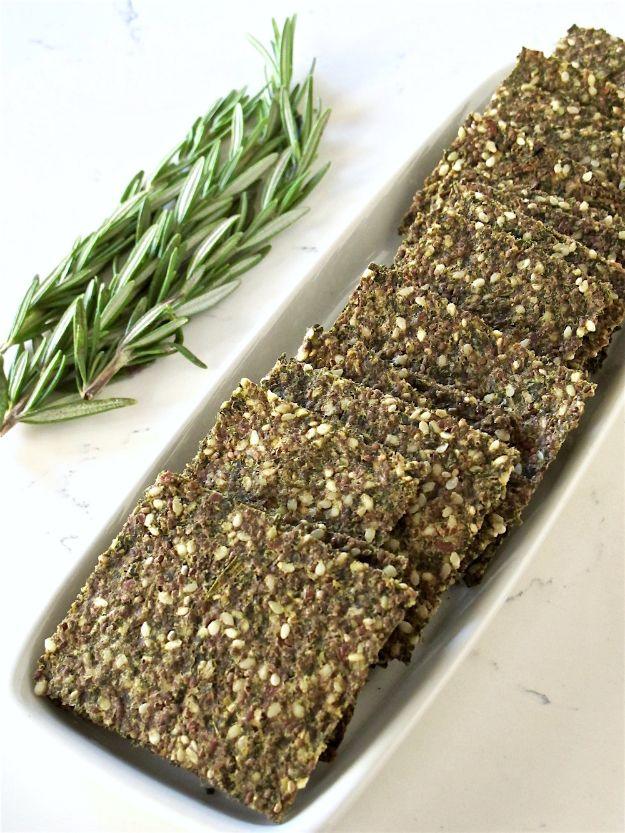 Kale rosemary seed crackers cut into rectangles on a long white platter with a bundle of fresh rosemary sprigs