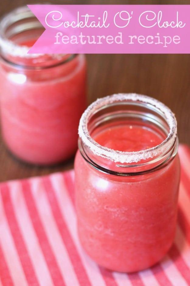 Creamy pink blended strawberry coconut margarita served in a sugar rimmed jar set on a pink striped cloth