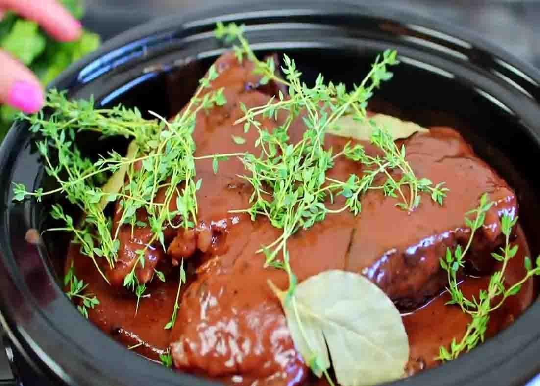 Putting the herbs over the pot roast in the slow cooker