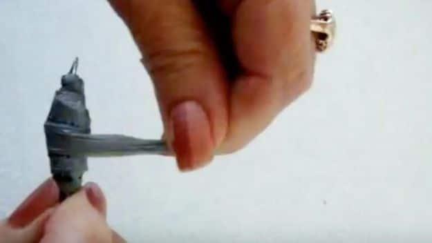 Hands rolling a strip of gray plastic bag into a bead, with the finished bead shaped on the end of the strip