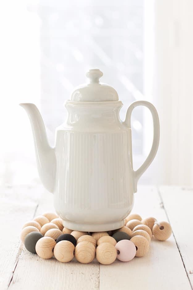 Wooden beads stained warm brown and strung on twine into a round trivet, sitting flat under a serving dish