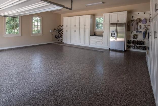Finished garage with a speckled gray flake epoxy floor, white cabinets, a refrigerator and a slat wall