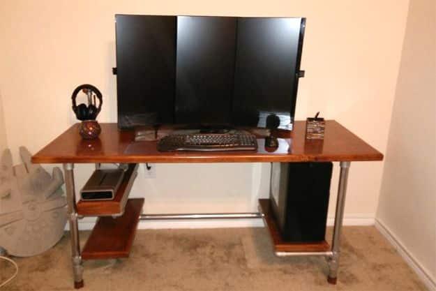Three monitor setup on a birch desk top built on a chrome pipe frame, with a lower shelf holding gear