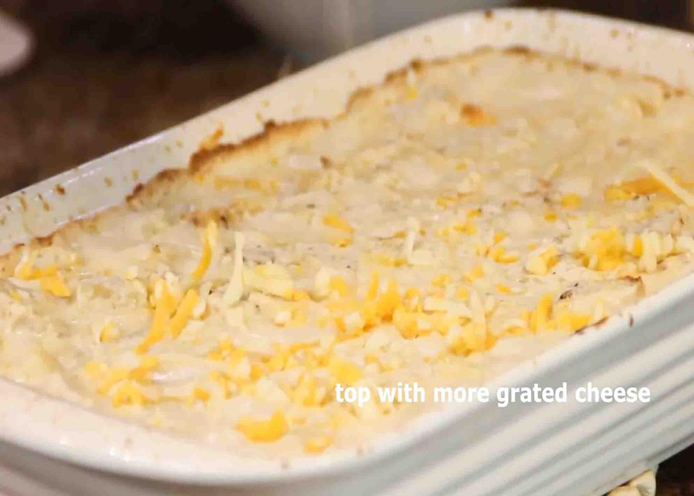 Sprinkling some more grated cheddar cheese over the chicken and potato casserole