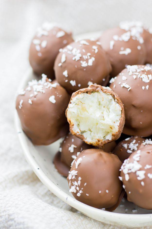 Chocolate dipped coconut truffles on a white plate with one bitten open to show the white coconut center
