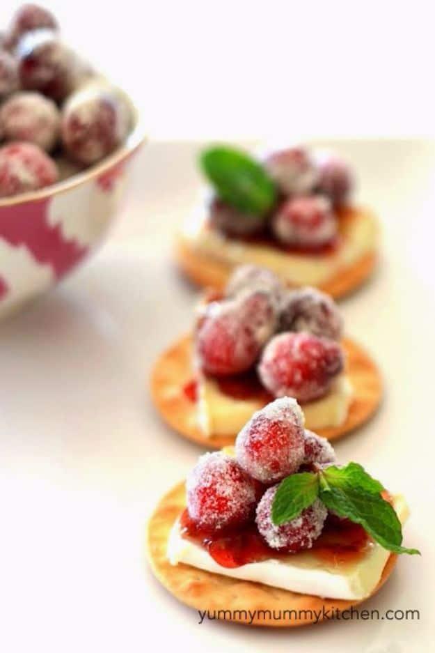 Sparkling cranberry brie bites on crackers with brie, cranberry chutney, sugared cranberries and mint leaves