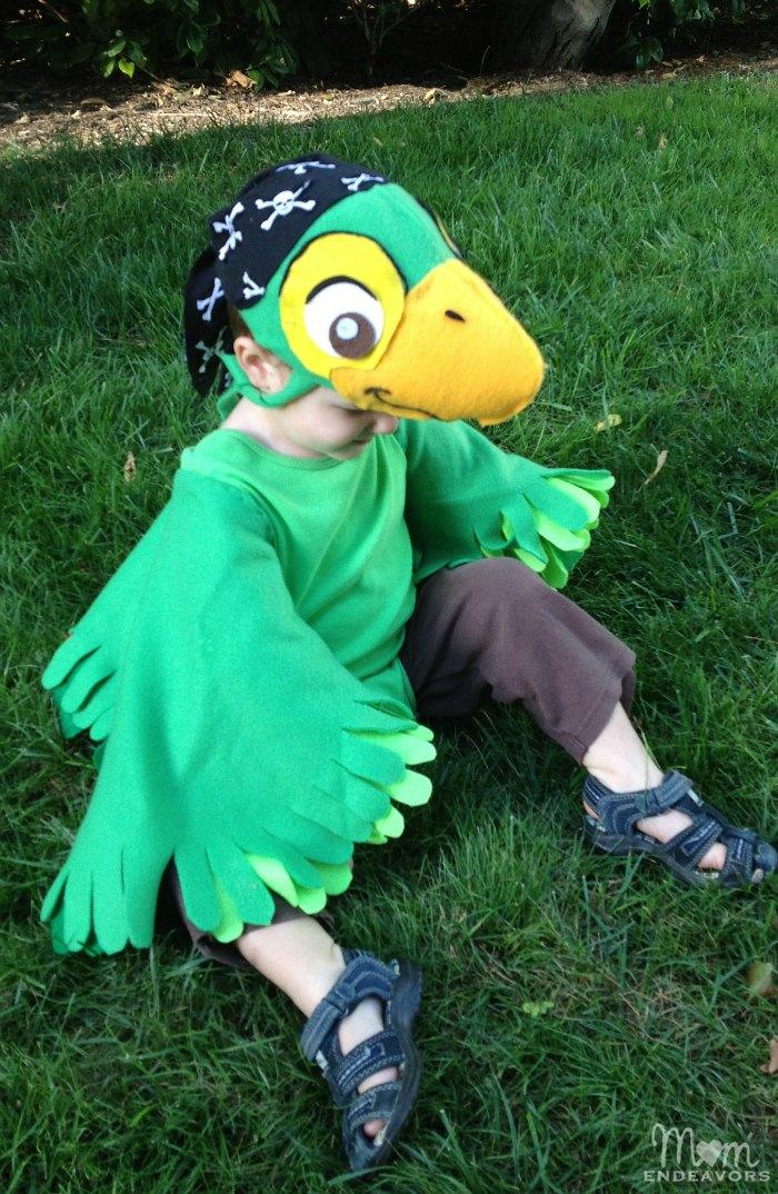 Child wearing a Skully parrot costume with green fleece wings, layered felt feathers and a matching pirate cap