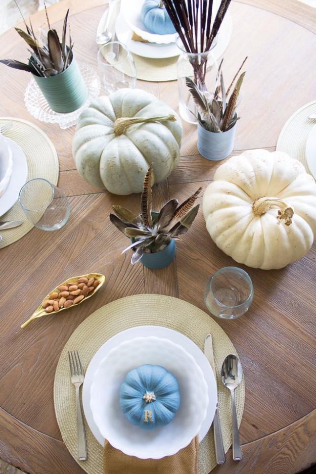 Thanksgiving table decor with chalk painted soup cans holding feathers and cattails beside painted mini pumpkins