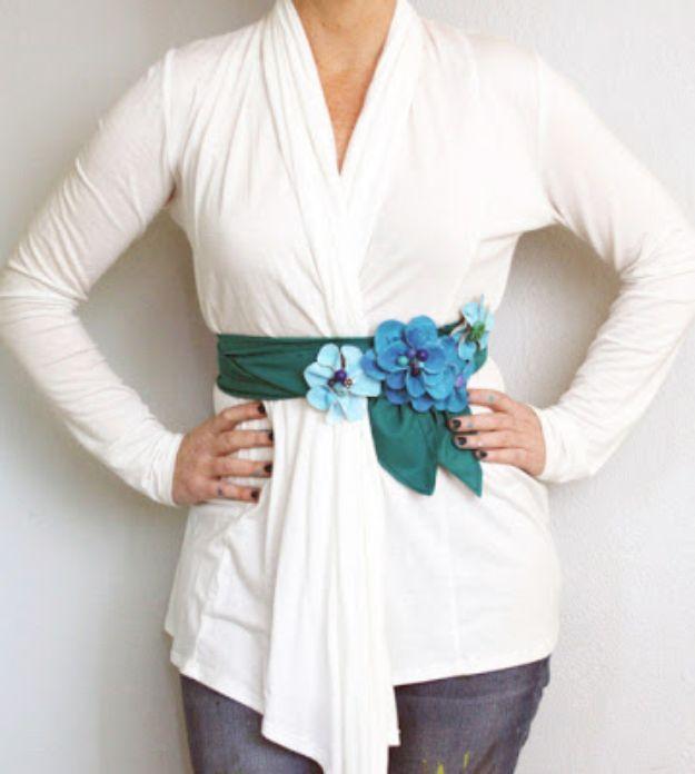 White wrap cardigan cinched with a deep green fabric sash carrying a cluster of blue and teal handmade canvas flowers