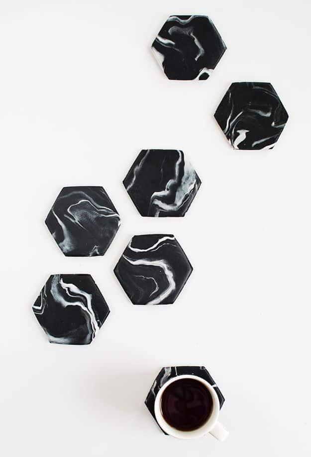 Four white marble hexagon coasters with gold-dipped edges, stacked on a dark tabletop beside a glass of iced water.