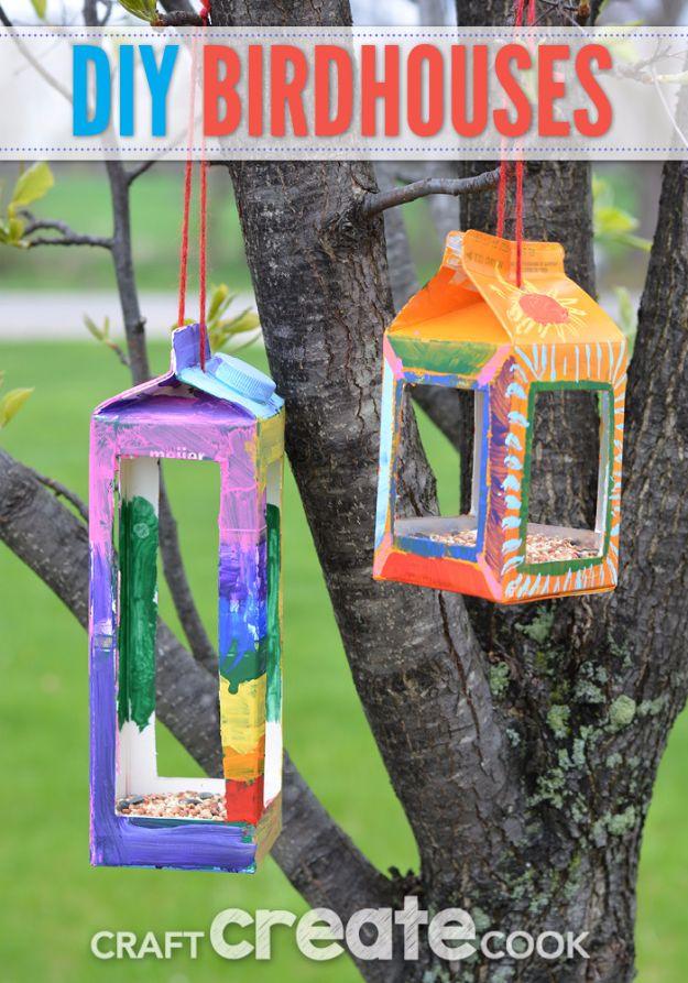Two milk carton bird feeders painted in bright colors, filled with birdseed and hung by red yarn in a flowering tree