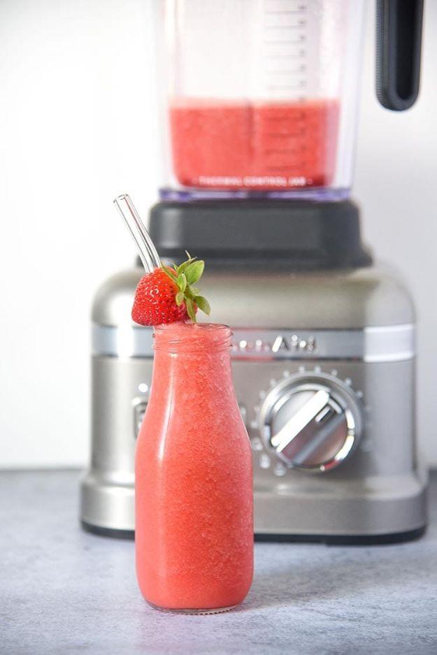 Strawberry watermelon juice in a glass bottle with a strawberry on top and the blender jar still behind it