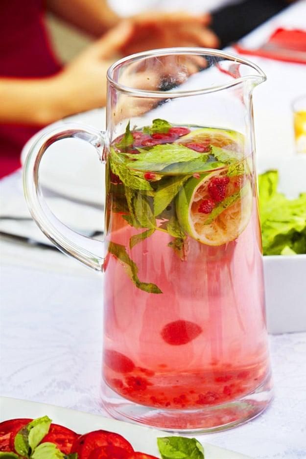 Glass pitcher of pink raspberry and mint scented water with fresh mint leaves, raspberries and strawberries