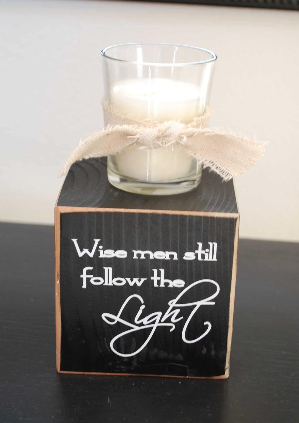 A black painted wood block lettered Wise men still follow the Light with a glass votive candle and a frayed canvas bow on top