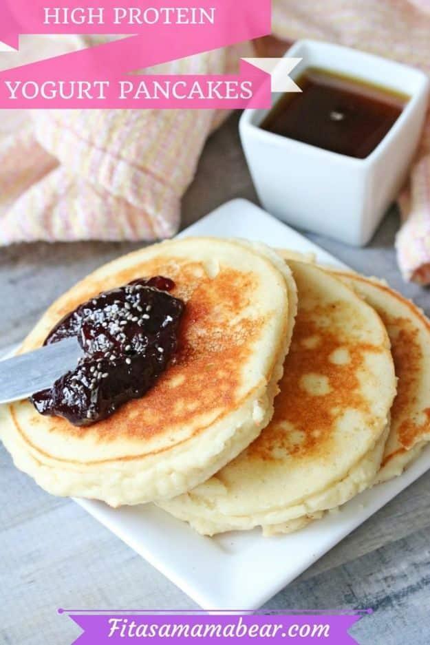 High protein yogurt pancakes on a white plate with jam spread across the top one and a dish of syrup