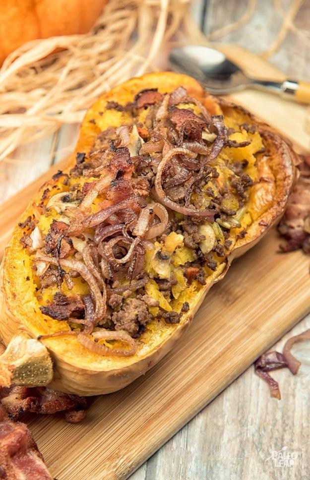 One butternut squash half on a wooden board stuffed with ground beef and vegetables, topped with crispy fried onions