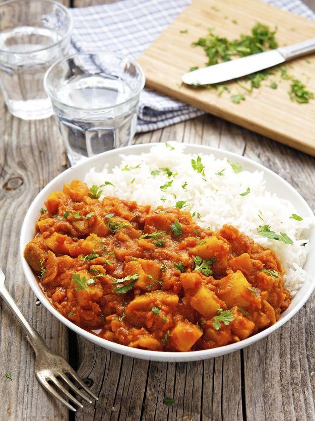 White bowl of orange pumpkin masala beside plain white rice, water glasses and a wooden chopping board