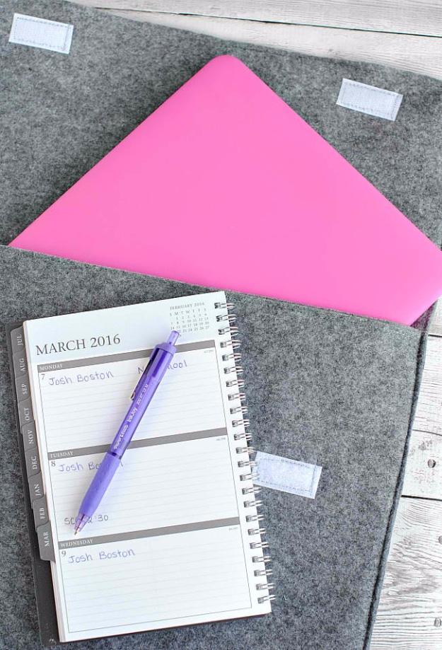 A thick mustard felt laptop sleeve cut to size with a snap closure, lying on a desk beside a notebook.
