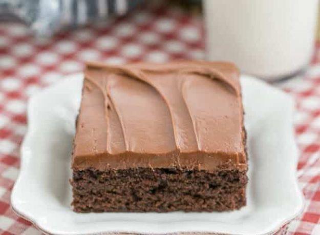 Cocoa fudge cake slice with thick chocolate buttercream frosting on a white plate over a red checked cloth