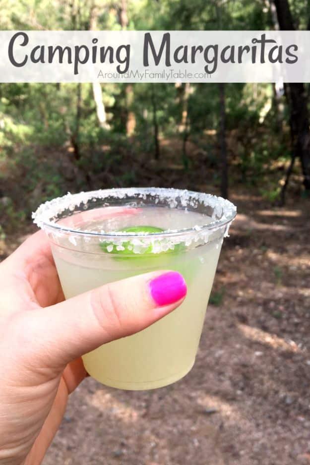 Hand holding a salt rimmed plastic cup of frozen margarita in a wooded campsite, under a typeset title