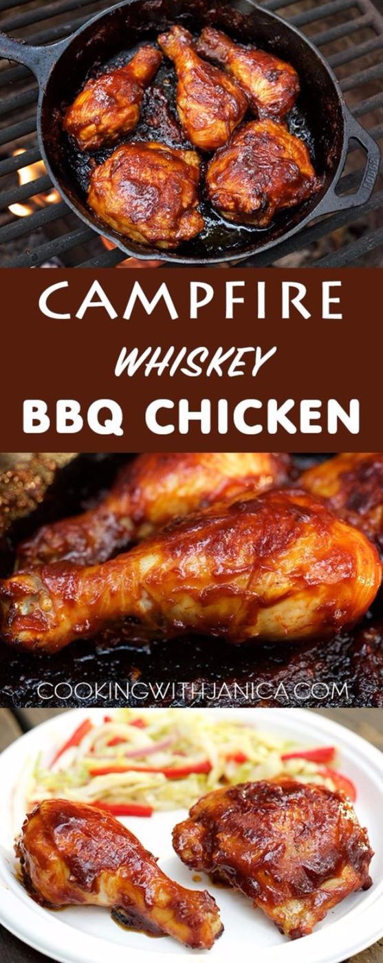 Campfire whiskey BBQ chicken legs and thighs cooking in a cast iron skillet over a wood fire on a cookout table
