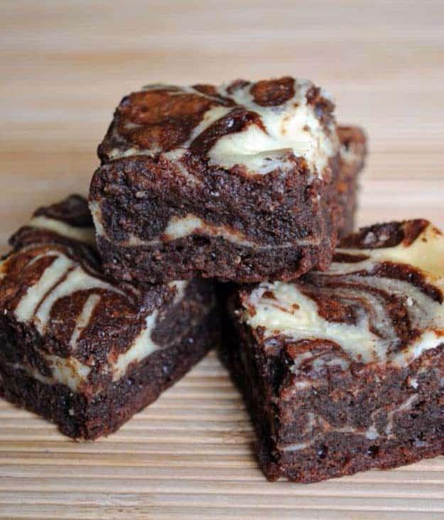 Whiskey cream cheese brownies stacked on a wooden board with a pale cream cheese swirl marbled on top