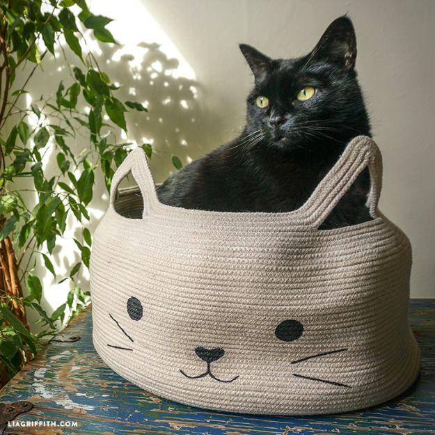 Rope bowl cat bed, a black cat sitting inside a coiled cotton rope basket with stitched whiskers and two ear handles