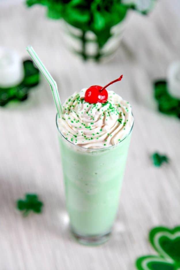 Homemade shamrock shake in a tall glass with whipped cream, green sprinkles and a cherry, shamrocks beside