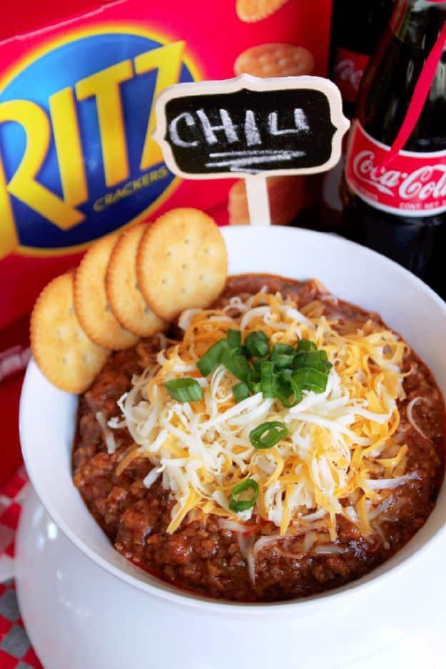 Coca Cola chili con carne in a white bowl under shredded cheese and green onion with Ritz crackers alongside