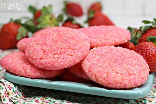 Pink strawberry champagne cookies rolled in sugar sprinkles stacked on a pale blue plate with fresh berries