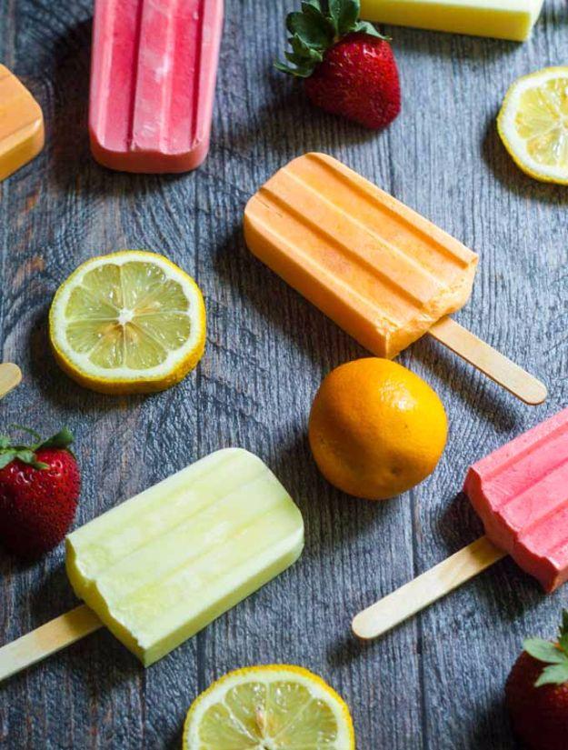 Pastel pink, orange and green creamy popsicles on grey wood with lemon slices and fresh strawberries