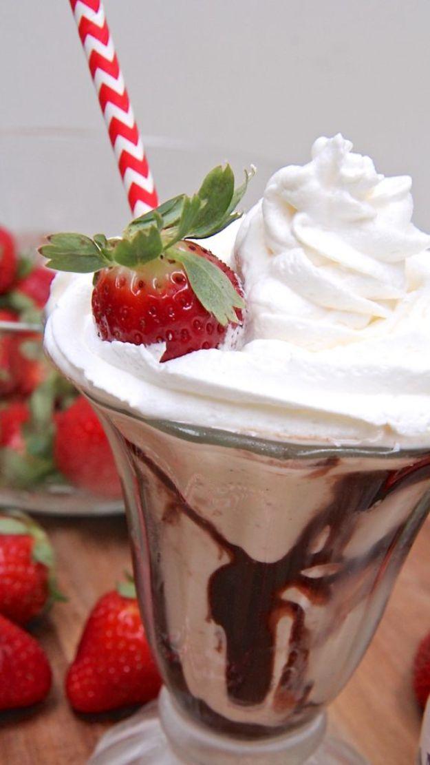 Boozy coffee milkshake in a tall sundae glass with fudge swirls, whipped cream, a strawberry and a red straw