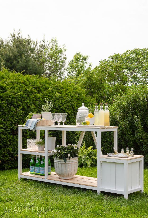 DIY outdoor bar painted white with natural cedar shelves, set on grass with lemonade jugs and a built in ice bin