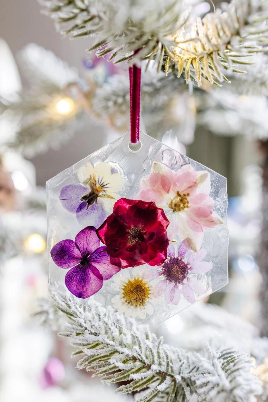Hexagon clear ornament with pressed pansies, a red rose and daisies sealed inside, hung by plum ribbon on a flocked tree