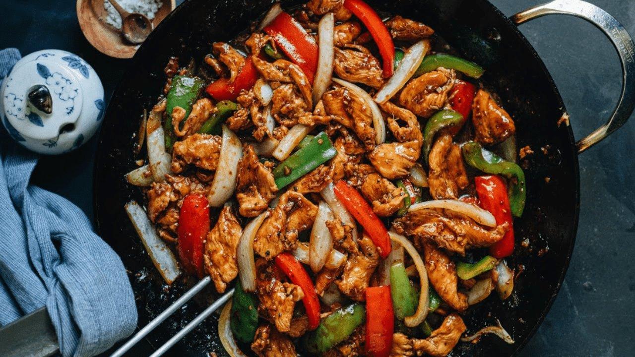 Skillet black pepper chicken with bell peppers and onion in a glossy dark sauce over rice, a dinner for one