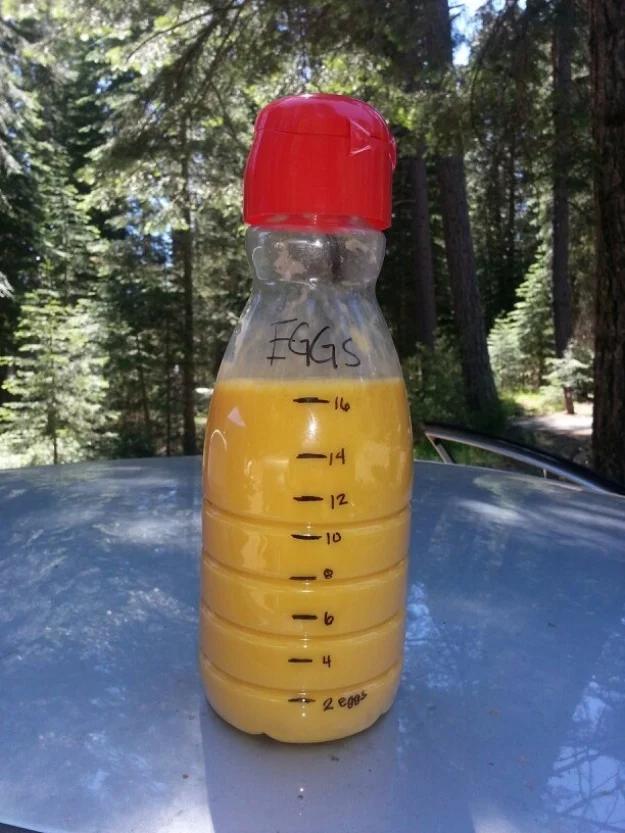 Clear bottle of beaten eggs marked with a hand drawn scale, standing outdoors against a forest backdrop