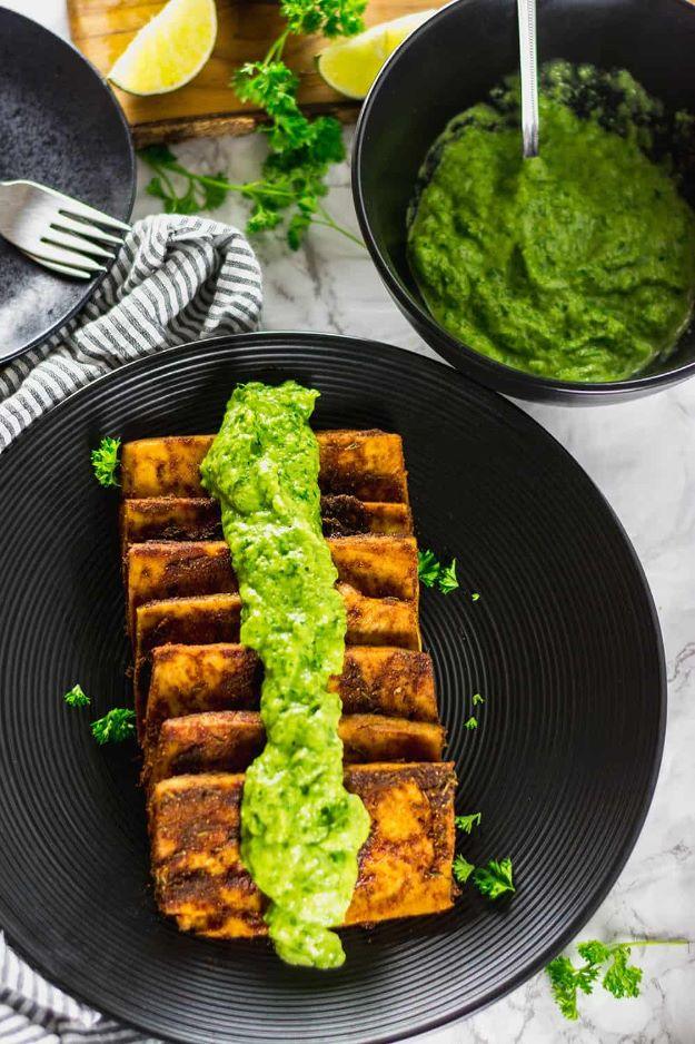Tofu steaks with avocado chimichurri, seared tofu slices on a black plate under a stripe of green sauce