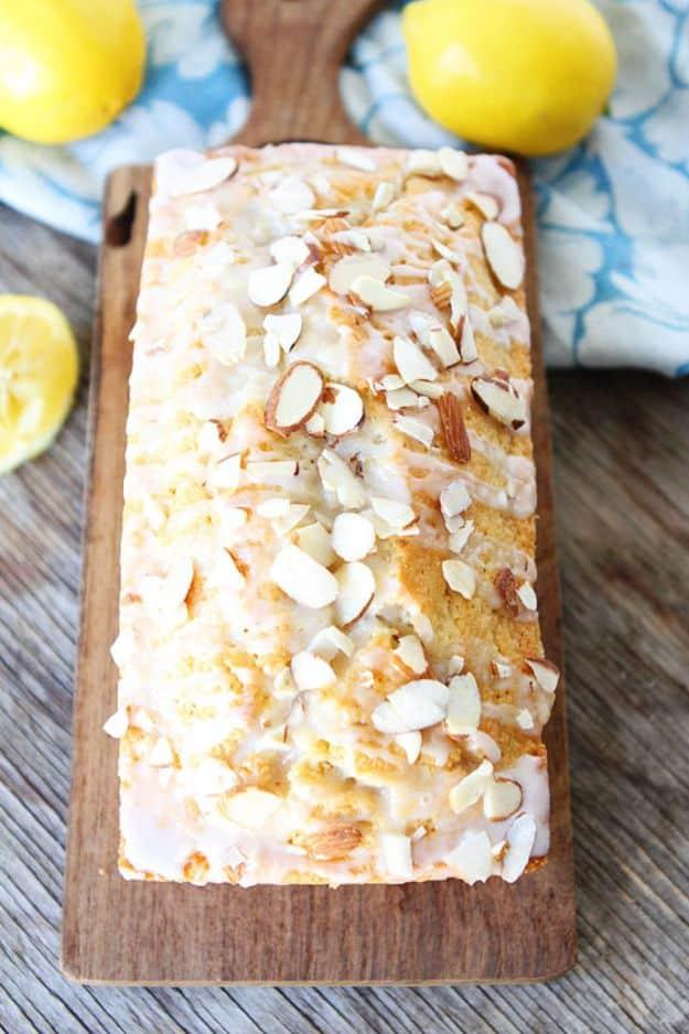 Lemon almond bread topped with sliced almonds and lemon glaze on a wooden board with fresh lemons beside it