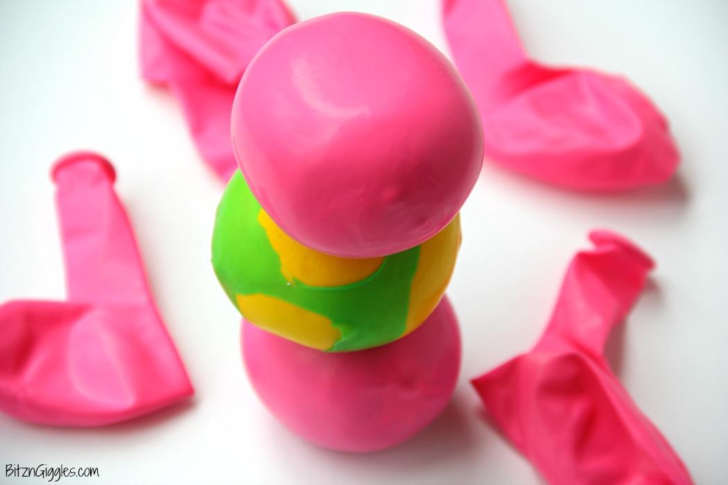 A pink and green balloon squeeze ball filled with flour sitting among loose pink balloons on a white background