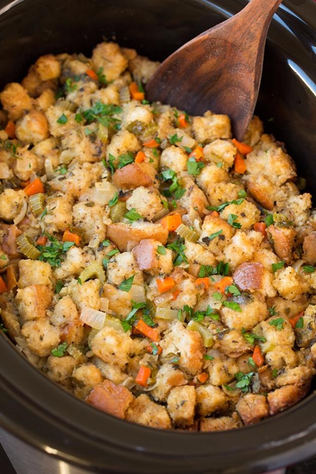 Golden bread stuffing with carrots, celery, herbs and a wooden spoon in a dark slow cooker for Thanksgiving
