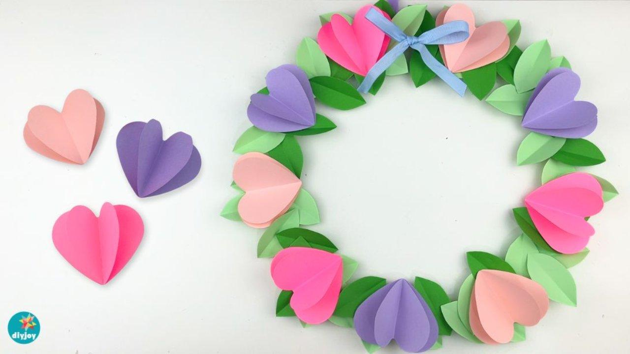 Paper heart wreath on a wooden hoop with folded 3D pink and purple hearts and green paper leaves for Valentine's Day