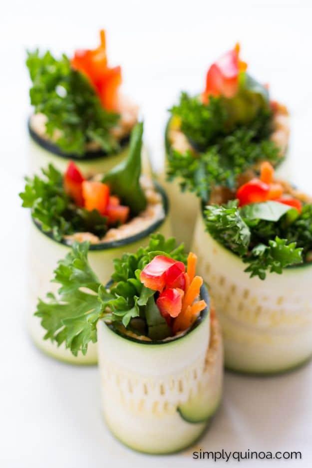 Zucchini roll ups standing upright filled with hummus and quinoa, topped with parsley and red pepper