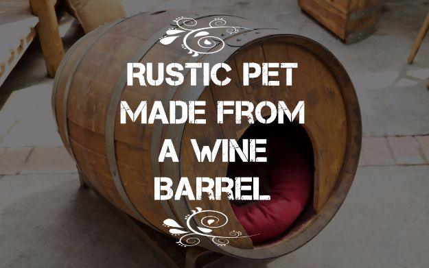 Rustic pet house made from a wine barrel laid on its side with one end open and a red cushion inside, on a patio