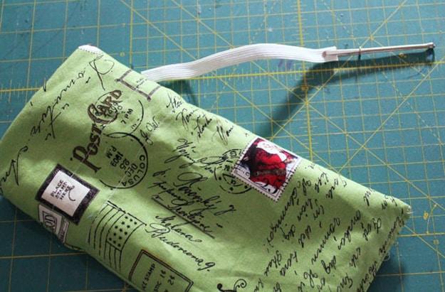 Use a bodkin to insert elastic, a green postcard print fabric casing on a cutting mat with a metal bodkin gripping white